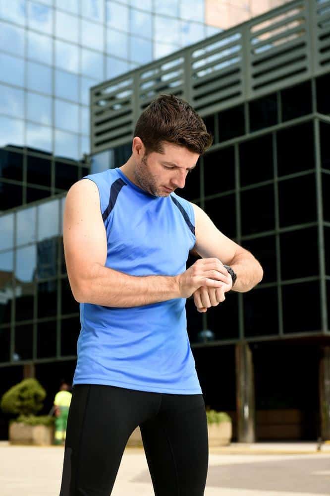 young sport man checking time on chrono timer runners watch holding water bottle after training session